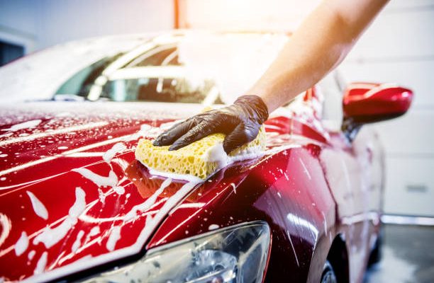 Worker washing red car with sponge on a car wash.